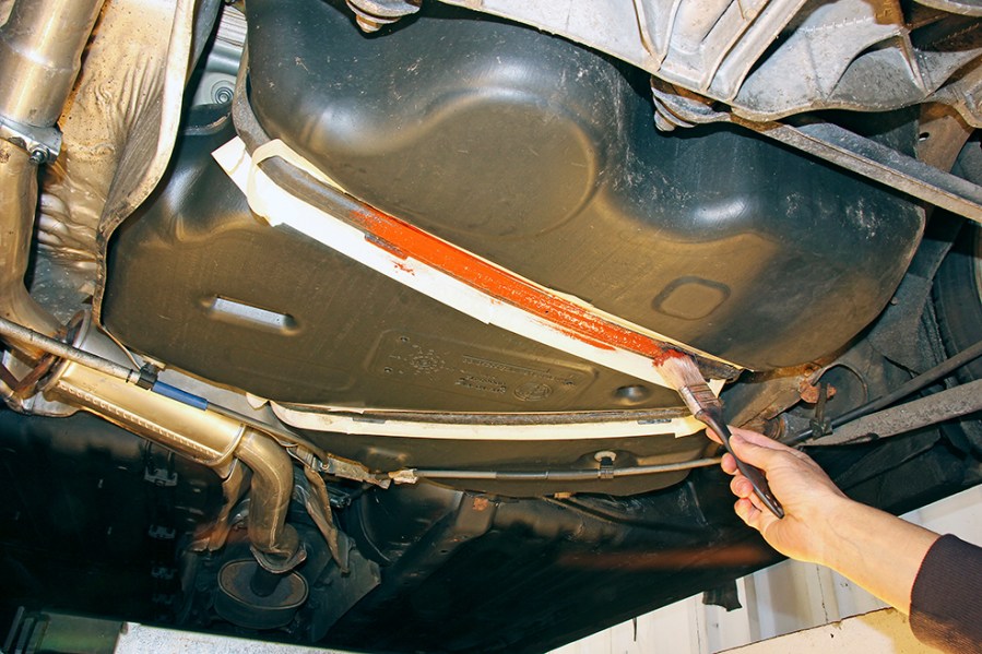 Once the rust cure solution has fully dried, apply a coat of metal primer. The surrounding areas may need to be covered, such as these tank straps, where the fuel tank doesn’t need to be painted, so it’s protected with masking tape.